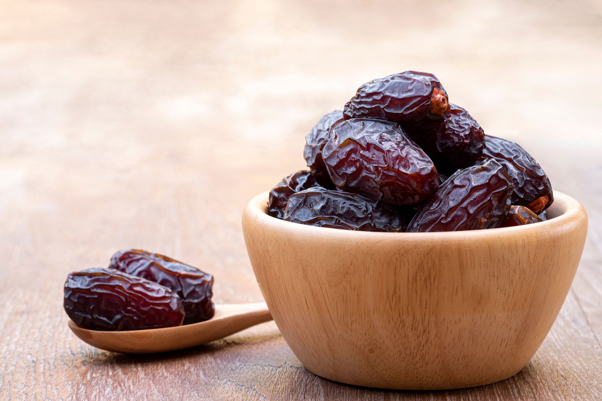 Plump Medjool dates in wooden bowl and spoon.